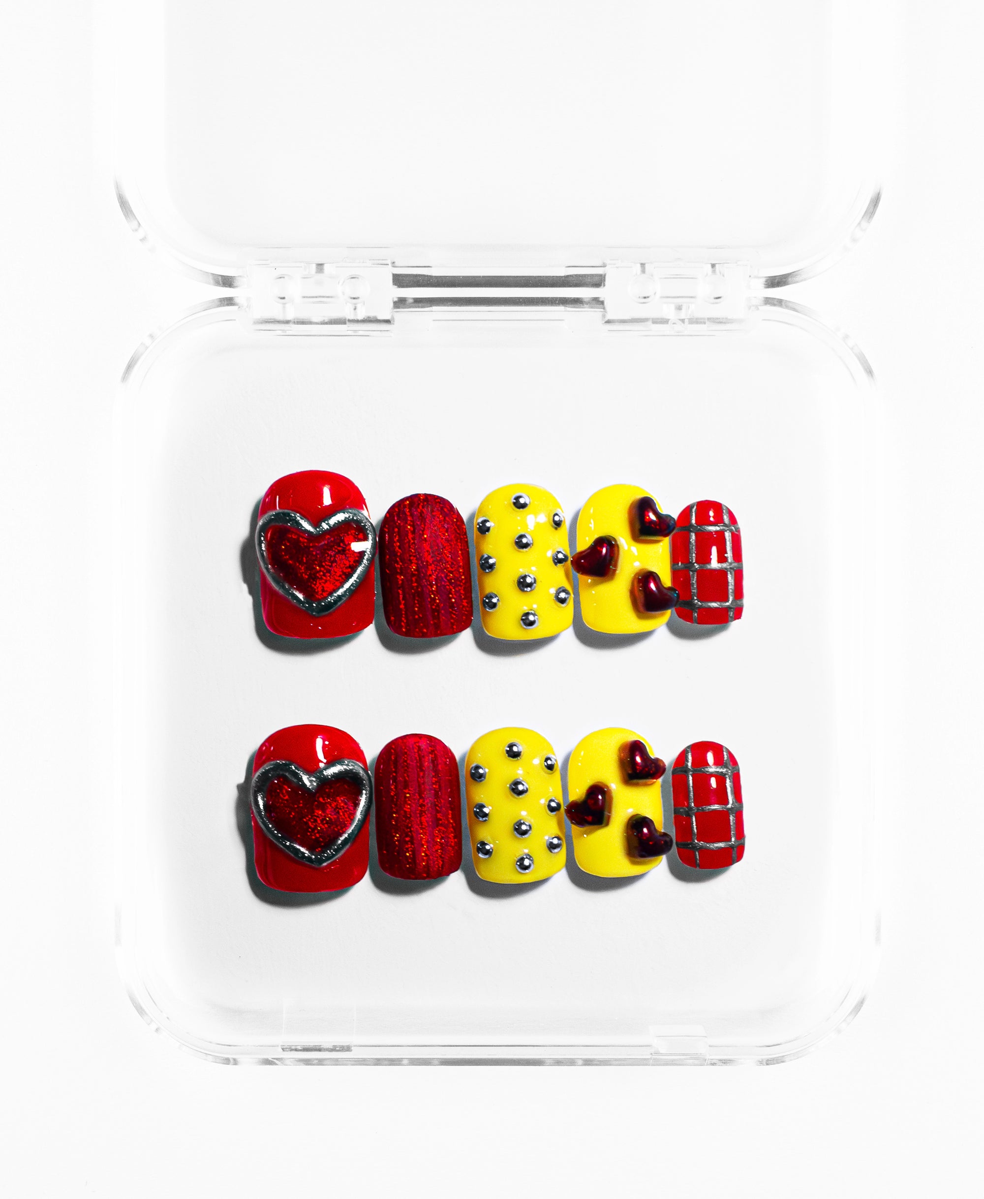 This press-on set features a bold mix of cherry red and sunny yellow in a square-oval shape. The collection is defined by its high-texture 3D elements, including a large shimmering red heart framed in silver, metallic silver studs, and clusters of tiny raised burgundy hearts. Finished with a classic red-and-silver grid pattern and a deep holographic red glitter nail, this set balances a playful, graphic aesthetic with an edgy, tactile energy.