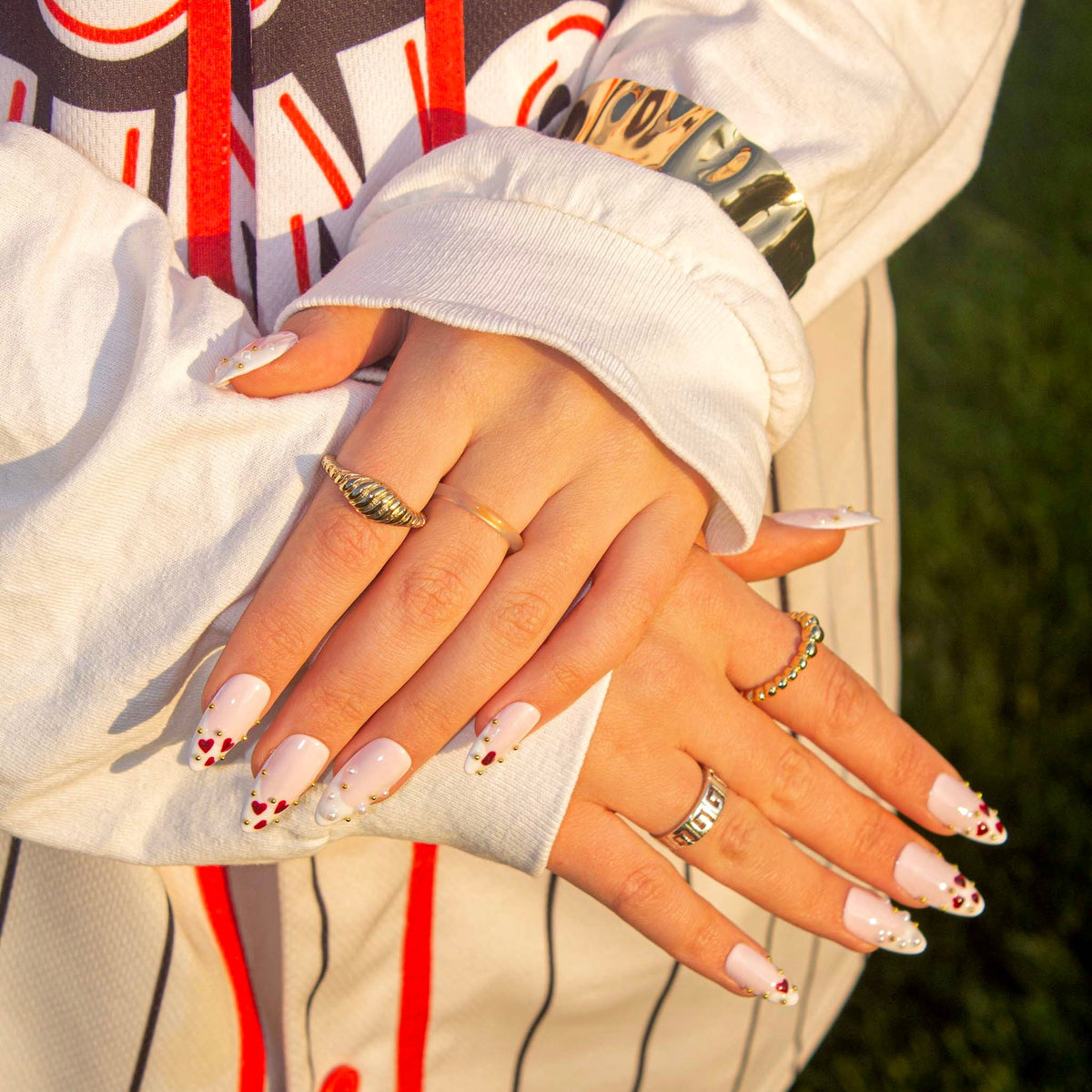 Love Notes press-on nails and gold rings over a striped baseball jersey