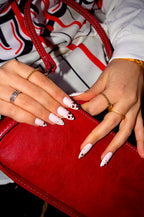 Love Notes press-on nails and stacked gold rings on a red leather bag