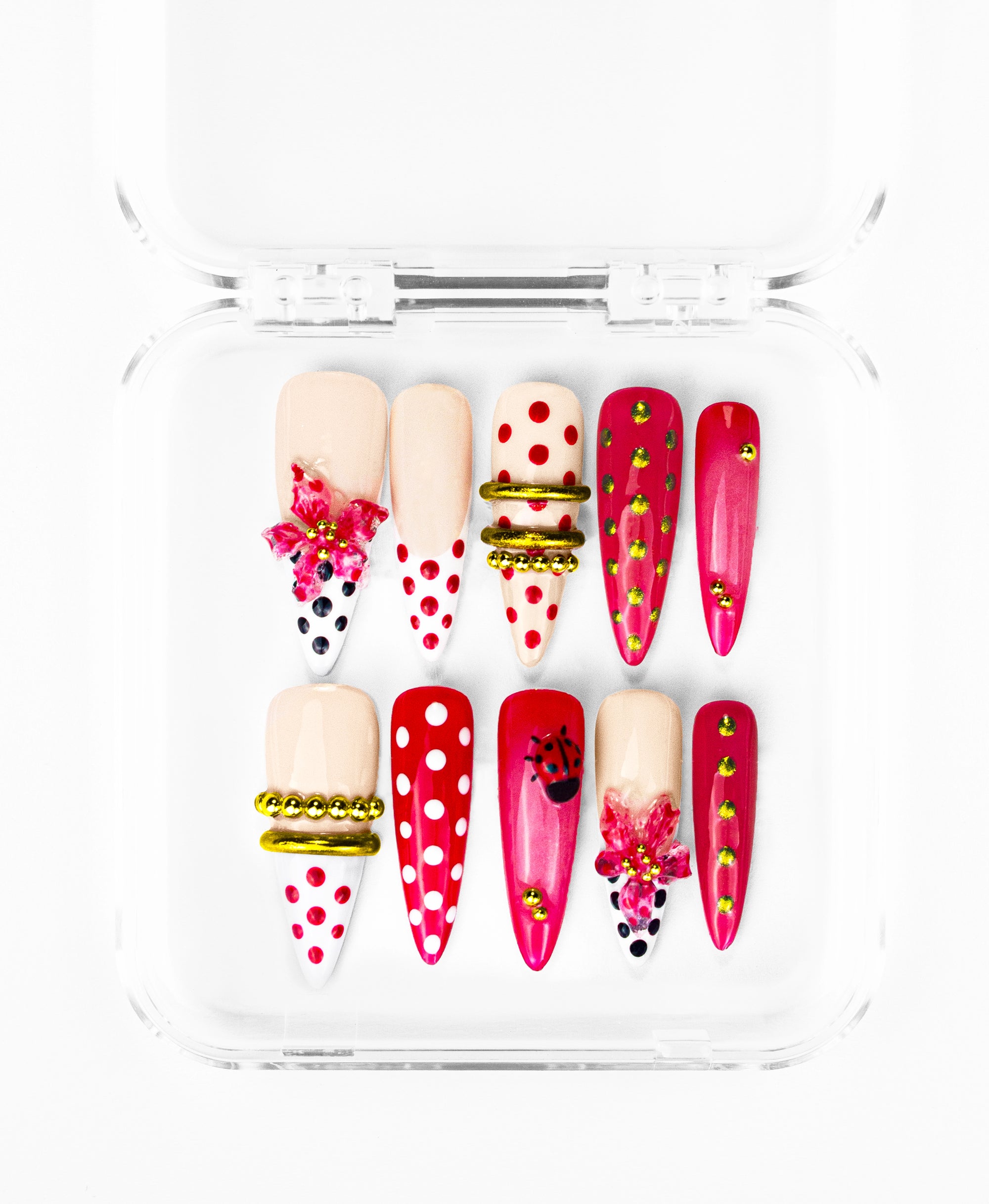 The long stiletto nails feature a mix of creamy nude and vibrant magenta bases, accented by playful ladybug 3D charms and shimmering pink floral gemstones. Striking gold bands and beaded rings divide the patterns, which range from crisp white-and-red polka dots to edgy magenta nails studded with lime-green rhinestones. The result is a high-contrast, maximalist design that balances whimsical nature motifs with a modern, structured look.