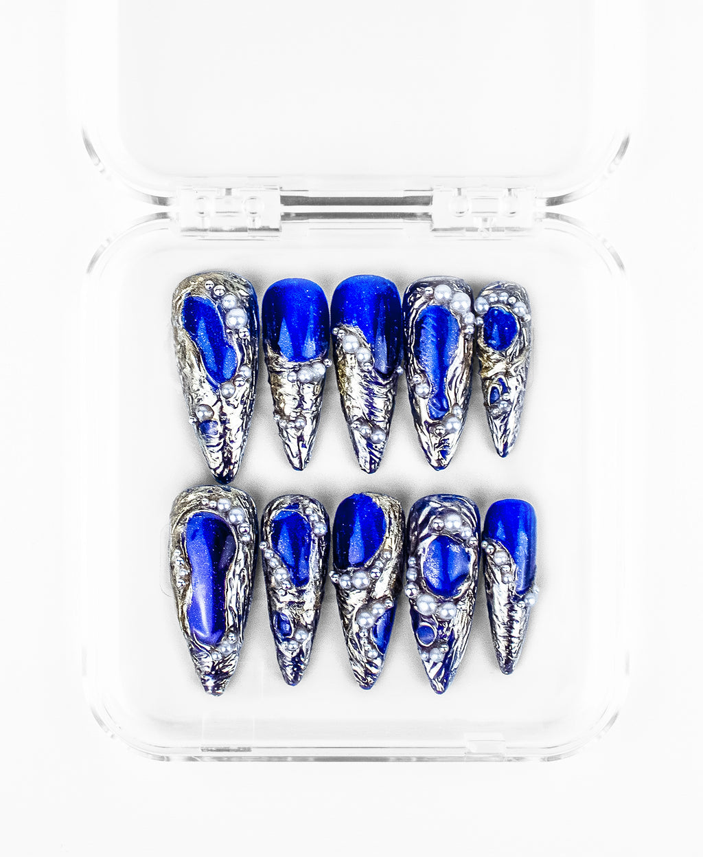 This press-on nails set features a striking, high-contrast aesthetic on sharp stiletto-shaped nails. The design is characterized by vibrant royal blue bases encased in heavily textured 3D silver "molten metal" frames that mimic flowing mercury. Scattered pearls of varying sizes are embedded into the silver textures, adding a touch of oceanic luxury to the edgy, sculptural hardware.
