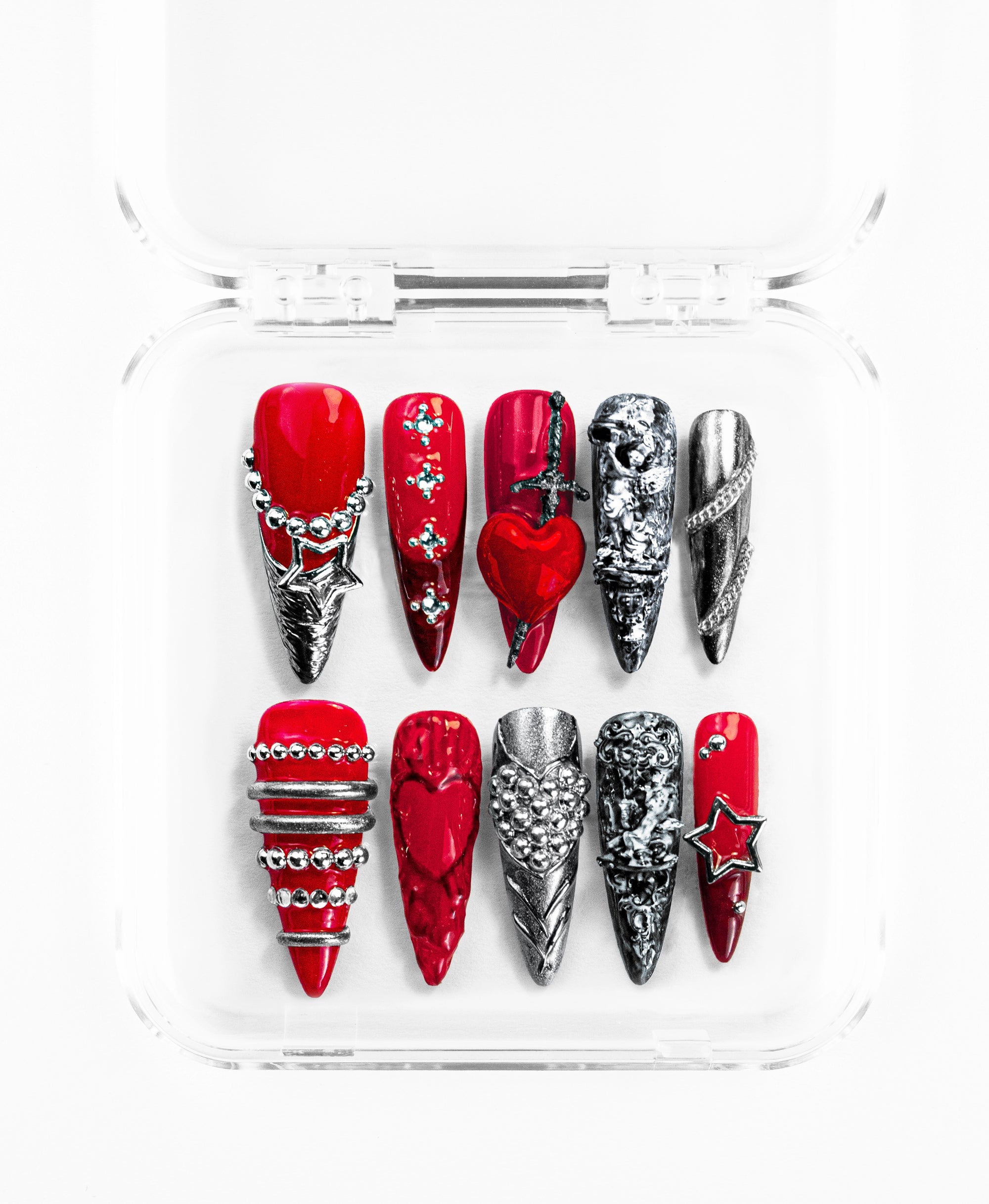 This stiletto-shaped press-on nail set features a striking gothic-romance aesthetic in vibrant cherry red and oxidized silver. Arranged in a clear case, the collection showcases intricate 3D details including a red heart pierced by a silver dagger, baroque-style carvings, metallic chains, and silver star charms. Blending rebellious hardware with romantic motifs, each nail is a textured masterpiece of studs, crosses, and embossed hearts.