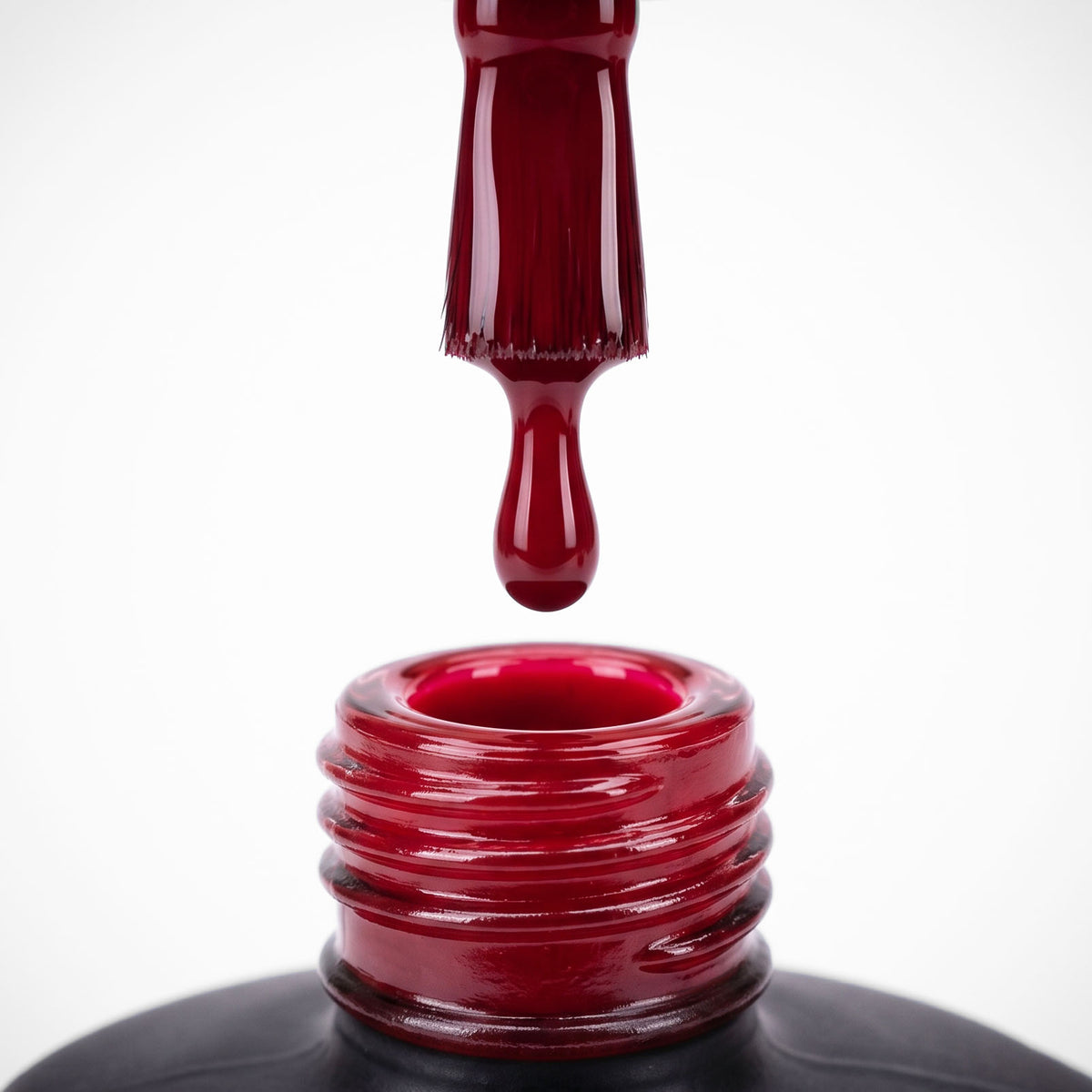 Nail polish brush lifted from an open bottle of deep red lacquer