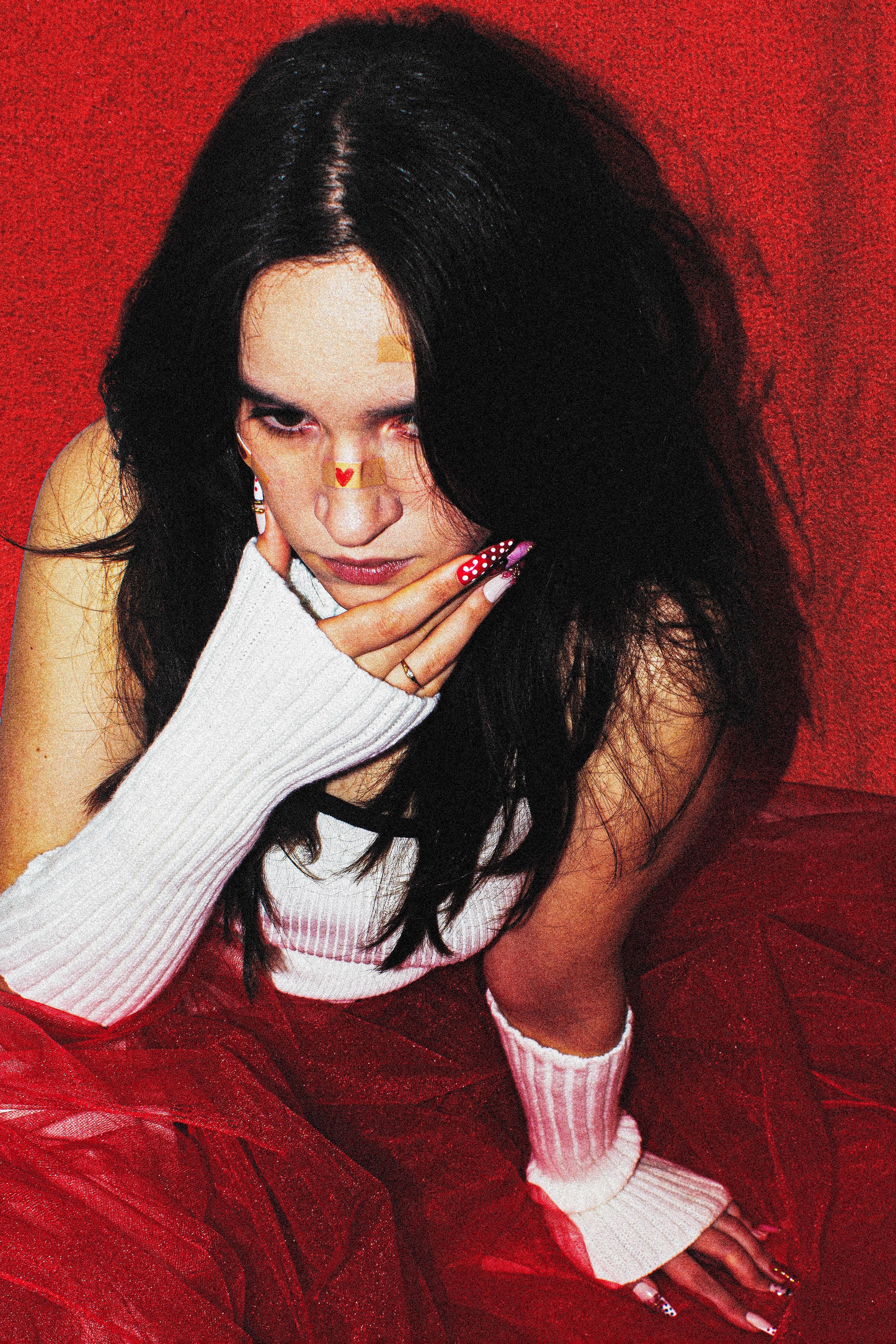 Person with long dark hair and white gloves sitting against a red background