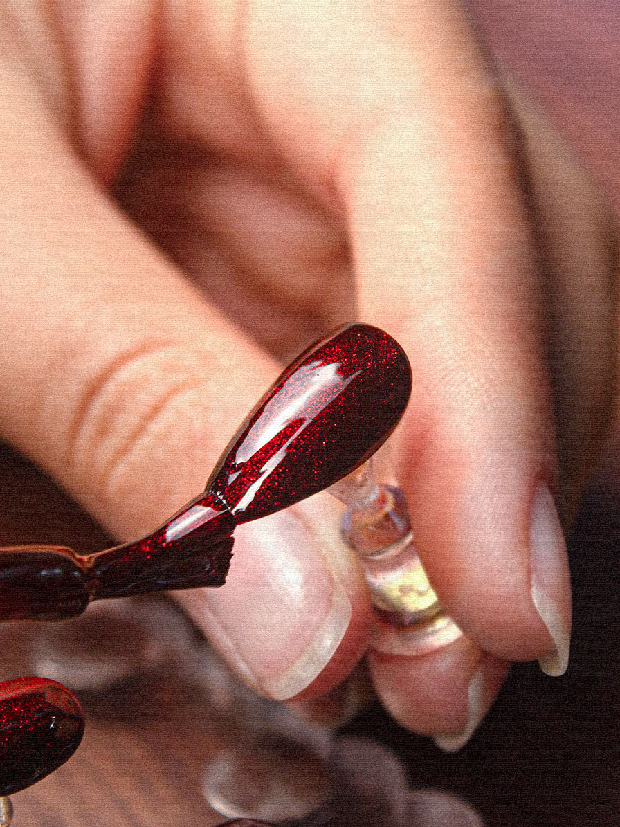 Macro of a hand-sculpted deep red beoopsie press-on nail held between fingers
