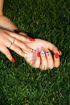Wildflower Berries strawberry press-on nails on hands resting in green grass