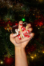 Hand holding a beoopsie Starfall press-on set in front of a Christmas tree