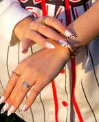 Close-up of Love Notes press-on nails with heart charms, rings and a baseball jersey