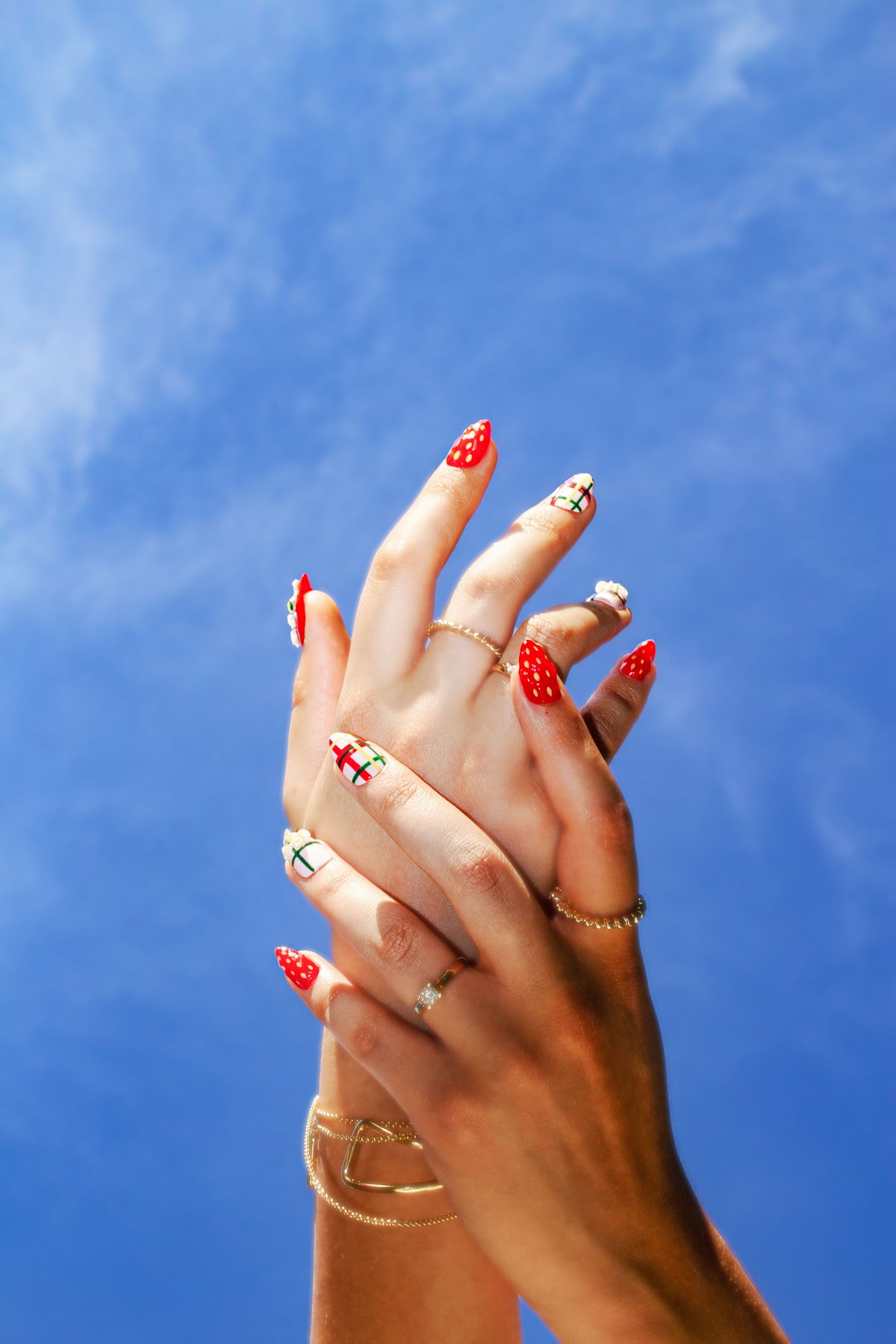 Strawberry press-on nails on clasped hands against a clear blue sky
