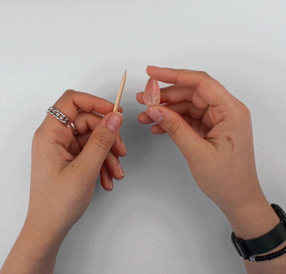 Scraping leftover adhesive off the back of a press-on nail with a cuticle stick